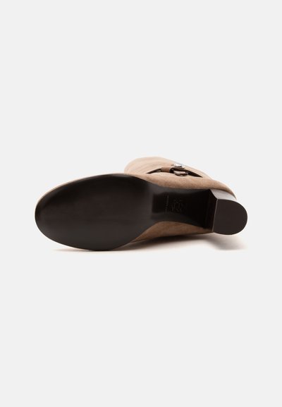 Bottine en daim marron posée sur le côté montrant une semelle noire lisse et un petit talon carré sur fond blanc.