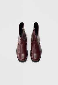 Botas de cano curto em couro bordeaux com acabamento liso, fecho de correr e sola de borracha. Apresentam um bico arredondado elegante e um design contornado.