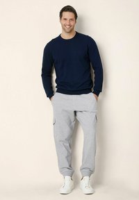 Marinblå crewneck-sweater i kombination med ljusgrå cargobyxor med sidofickor, kompletterad med vita sneakers på en neutral bakgrund.