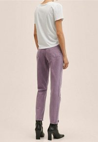 Jeans de mezclilla morados con un corte ajustado, bolsillos traseros y costuras en contraste, combinados con una camiseta de algodón blanca y botas de tacón negras.