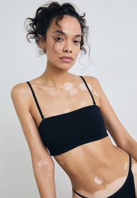 Haut bandeau noir avec des fines bretelles, fabriqué en tissu doux. Présente une texture lisse et un design simple et minimaliste.