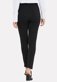 Zwarte slim fit broek met een gladde textuur, voorzien van achterzakken en een hoge tailleband, gecombineerd met zwarte hoge hakken sandalen.