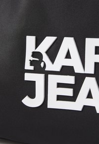 Black fabric bag featuring a large white embossed logo that includes the text "KARF JEAN" with a cutout design detail.
