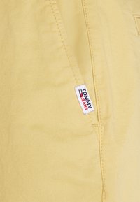 Tessuto di cotone giallo con una superficie liscia; presenta un'etichetta Tommy Jeans con accenti rossi e blu cucita di lato.