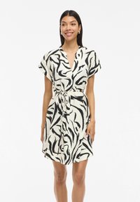 Kurzärmeliges Kleid aus einem cremefarbenen Stoff mit einem schwarzen abstrakten Zebradruck, V-Ausschnitt und einer taillierten Detail mit Schleife.