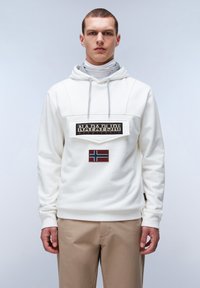Sudadera blanca con capucha y un gran parche negro que muestra el texto "NAPAPIJRI geographic" y un emblema de la bandera de Noruega en rojo y azul en la parte delantera.