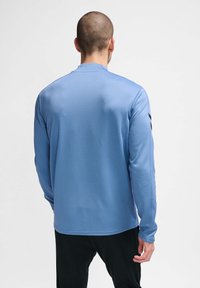 Langsleeve sportshirt van lichtblauwe stof, heeft een gestructureerd patroon en zwarte strepen langs de mouwen, met een rechte zoom.