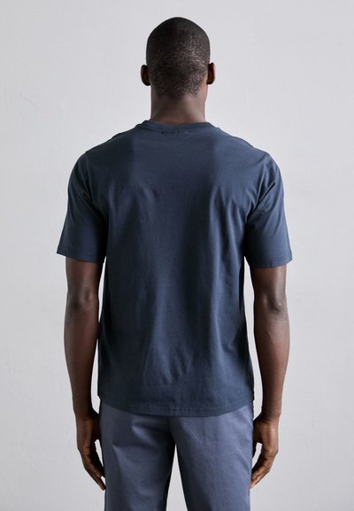 Camiseta de algodón azul marino con cuello redondo y mangas cortas. Presenta un corte relajado y un dobladillo trasero ligeramente más largo. Diseño minimalista.