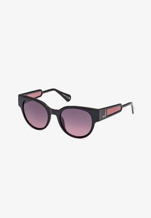Gafas de sol negras con forma redondeada, lentes degradados en color púrpura, brazos planos en negro y acentos rojos en las patillas. Incluye el logo de la marca en el lateral.