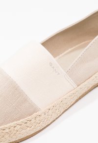 Gros plan d’une espadrille en toile beige avec une semelle en jute tressée et un logo GANT discret sur la partie supérieure.