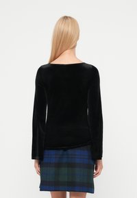 Top negru din catifea cu mâneci lungi și decolteu rotund, asortat cu o fustă în carouri în tonuri de verde, albastru și negru, prezentat din spate.