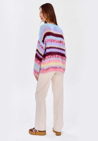 Dzianinowy sweter w pastelowe paski w kolorach niebieskim, różowym, lawendowym i bordowym. Posiada luźny krój oraz szerokie rękawy. W zestawie z jasnymi spodniami.