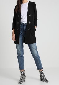 Černý dlouhý kabát se šesti velkými knoflíky, doplněný světle modrými džínami a kotníkovými botami se vzorem zebry. Pod tím bílý tri�čko.