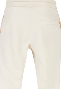 Pantalones de chándal color crema con cintura elástica, que cuentan con un único bolsillo trasero y una textura suave y lisa.