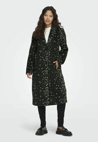 Lungo cappotto nero con un motivo a stampa leopardata verde, due tasche frontali, design doppiopetto e una texture liscia. Abbinato a pantaloni e scarpe nere.
