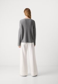 Grijze gebreide trui met ribbelstructuur, gecombineerd met wijde witte broek. De outfit heeft lange mouwen en een ontspannen pasvorm.