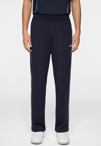 Marina atletiska byxor med elastisk midja, sidostråk och en logotyp på vänster höft. Tillverkade av ett mjukt, lätt tyg.