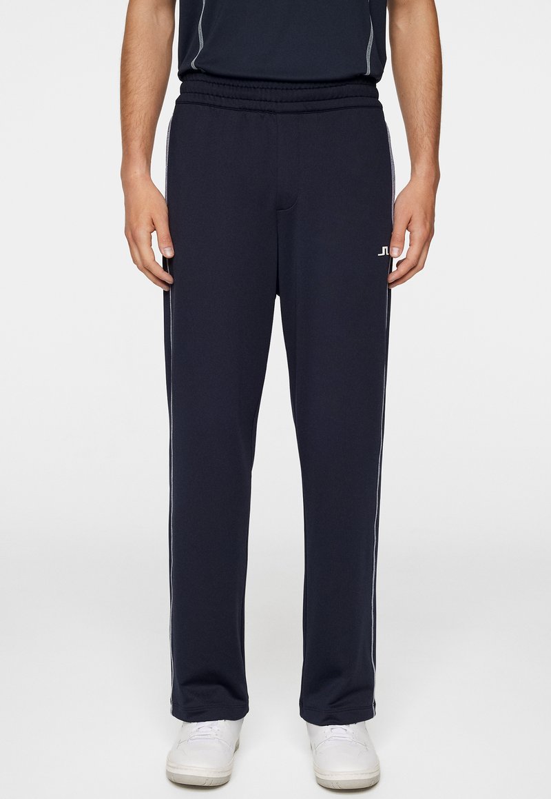 Marina atletiska byxor med elastisk midja, sidostråk och en logotyp på vänster höft. Tillverkade av ett mjukt, lätt tyg.