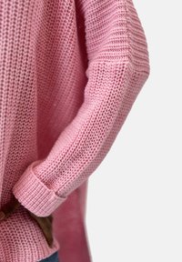 Stickad rosa tröja med en strukturerad väv, ribbade ärmmuddar och en avslappnad passform, med synliga sömmar och en något sänkt axeldesign.