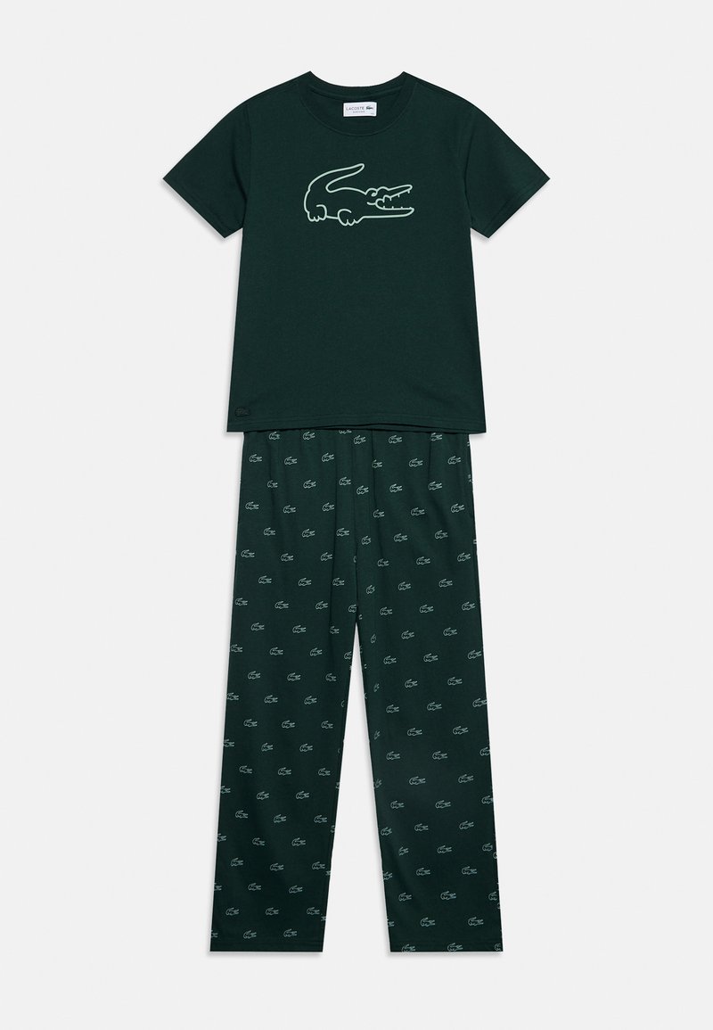 Chemise à manches courtes vert foncé avec grand logo crocodile, associée à un pantalon vert foncé assorti avec petits logos crocodile répétés.