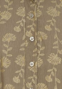 Brun stofskjorte med et gyldent blomstermønster og tekstureret detaljer. Den har en knaplukning foran med sølvknapper og en blød tekstur.