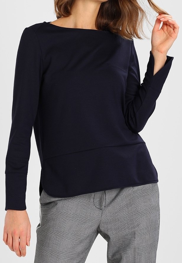 Tmavě modrý top s dlouhým rukávem a lodním výstřihem, těsně přiléhavý střih a boční rozparky, kombinovaný se šedými károvanými kalhotami. Hladká textura tkaniny.