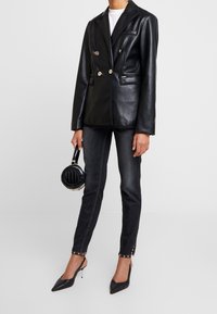 Black leather double-breasted blazer with gold buttons, dark grey skinny jeans with gold accents, and a round black handbag. Black pointed heels.