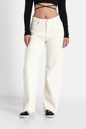 Jeans de mezclilla blanca de pierna ancha con un dobladillo deshilachado y bolsillos delanteros, combinados con un top corto negro de canalé. Los zapatos son zapatillas negras con suelas blancas.