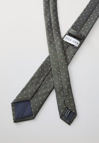 Cravate en soie vert foncé avec un motif en chevrons et de petits accents roses ; elle présente un tissu bleu marine à la pointe et une étiquette portant la mention "PIER.ONE."