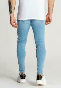 Jeans skinny azul claro fabricados en denim, con un ajuste ceñido y un diseño minimalista, combinados con unas zapatillas de moda en blanco y negro.