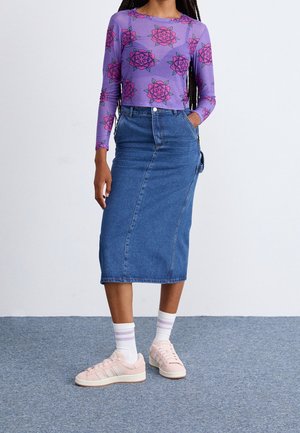 Kvinde iført en lilla langærmet top med pink blomsterprint, en højtaljet blå denim midi-nederdel, hvide sokker og lyserøde sneakers.