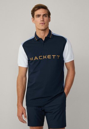 Polo a manica corta blu navy e bianco con colletto, caratterizzato dal logo dorato "HACKETT" sul petto e un design a contrasti sulle spalle.