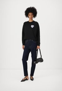 Felpa nera con un logo bianco a forma di cuore contrassegnato "HUGO", abbinata a jeans slim blu scuro e ballerine nere. Accessoriato con una piccola borsa nera.