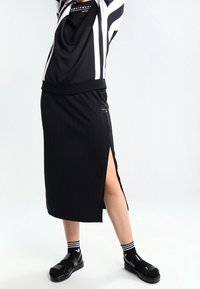 Svart ribbad midikjol med sidoklyfta. Matcher med en svart och vit randig topp och svarta sandaler. Strukturerad tyg med en sportig design.