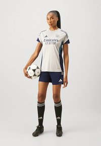 Szary i granatowy strój piłkarski z napisem "Emirates Fly Better", granatowe spodenki, czarne skarpety w białe paski oraz czarne korki piłkarskie. Trzyma piłkę nożną.