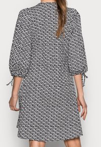 Kraťasové šaty černobílé vzorované s nafouklými rukávy a vázacími detaily, mají volný střih a lem, který končí nad koleny.