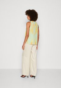 Top sin mangas de color azul claro con patrón abstracto amarillo; combinado con pantalones de pierna ancha color crema y tacones negros destalonados. Tela texturizada.