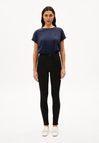 Camiseta azul marino con mangas enrolladas, acompañada de jeans negros de cintura alta. Unos zapatos slip-on de tejido blanco completan el conjunto.
