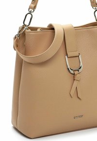 Bolso de mano de cuero beige con textura, con una correa desmontable, herrajes de metal plateado y un detalle decorativo en forma de lazo en la parte frontal.