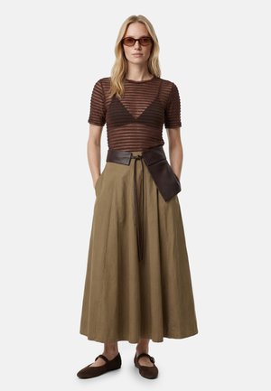 Kobieta ubrana w brązowy, paskowany przezroczysty top, czarny bralette, długą oliwkową spódnicę, szeroki ciemnobrązowy pasek z kieszonką, brązowe baleriny i okulary przeciwsłoneczne.