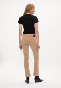 Zwarte cropped t-shirt en beige corduroy flare pants met dubbele achterzakken. Zwarte enkellaarsjes. Soepele stofstructuur, minimalistisch ontwerp.
