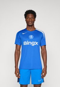 Blå Nike fodboldtrøje med korte ærmer, der har et rundt logo og teksten "Bingx". Kombineret med matchende blå shorts. Glat tekstur.