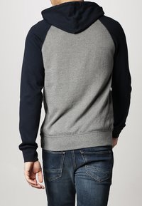 Bluza z kapturem o szarym korpusie i granatowych rękawach. Posiada kieszeń kangurkę oraz ściągacze na rękawach. Wykonana z materiału bawełnianego z gładką fakturą.