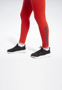 Czerwone legginsy sportowe z bocznymi szwami i czarnym logo "Reebok". Czarne buty sportowe z teksturowanym chwytem i białą podeszwą.