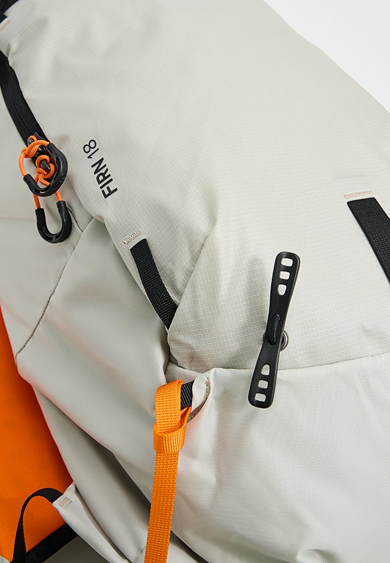 Mochila exterior de color gris claro con correas negras, detalles en naranja y cierres de toggles. Tela texturizada con un acabado suave y logo.