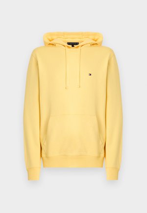 Sárga kapucnis pulóver puha anyagból, elülső kenguruzsebbel, húzózsinóros kapucnival és kis logóval a mellrészen.
