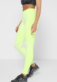 Leggings de tiro alto, de un brillante color amarillo neón, con paneles texturizados y un pequeño logo negro de Nike en el lateral. Material suave y elástico.