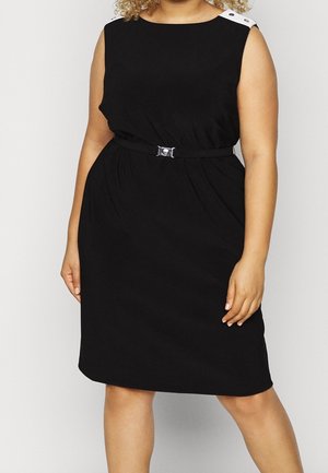 Femme portant une robe noire sans manches avec des boutons blancs aux épaules et une fine ceinture noire à la taille.