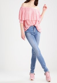 Top rosa scollato con strati di rouches, jeans skinny blu chiaro e sneaker rosa con dettagli in pelliccia. Un outfit semplice e casual.