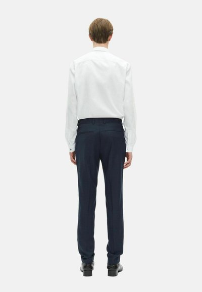 Biała koszula z długim rękawem zestawiona z ciemnoniebieskimi spodniami o dopasowanym kroju i czarnymi butami, widok z tyłu. Gładki materiał, dopasowany krój.